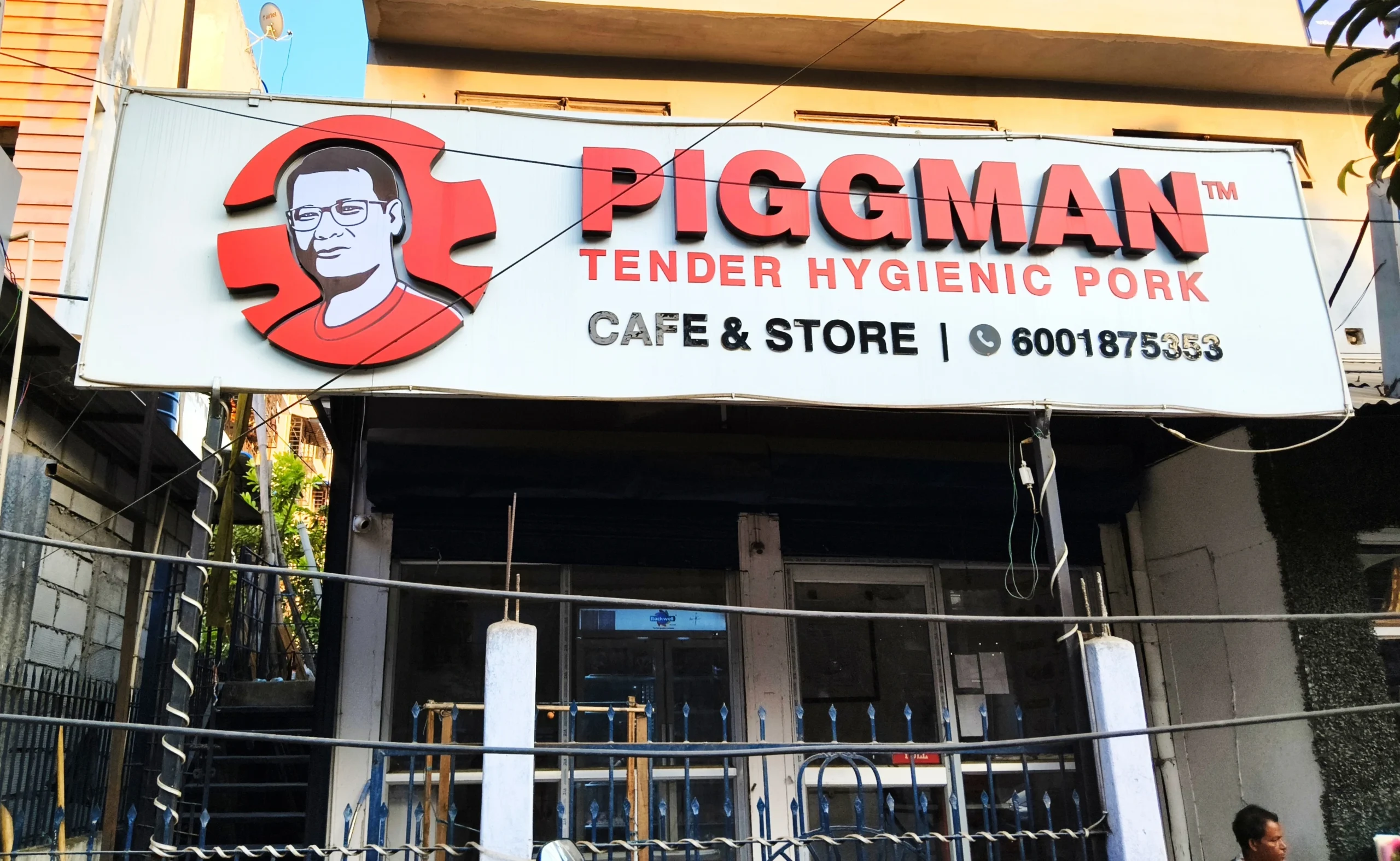 Front facade of a Piggman outlet displaying the Piggman logo and signage reading ‘Piggman Tender Hygienic Pork – Cafe & Store’, with the storefront and surrounding street visible.