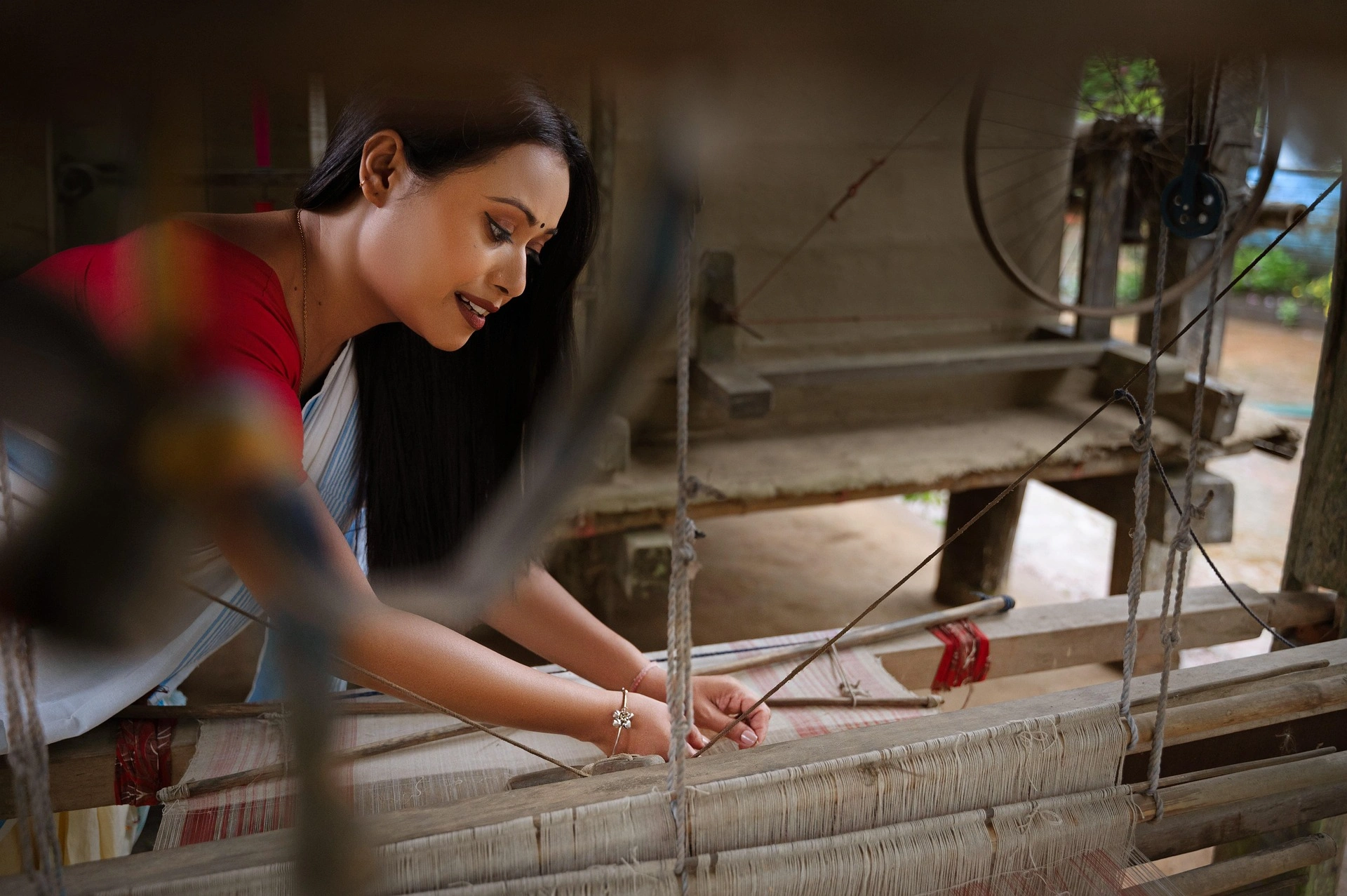 An Assamese weaver inspecting the threads on a traditional loom before starting the weaving process.