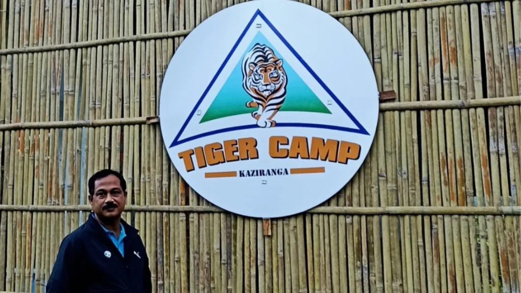 Amitabh Sarma standing beside the Tiger Camp Kaziranga sign at the bamboo-walled property